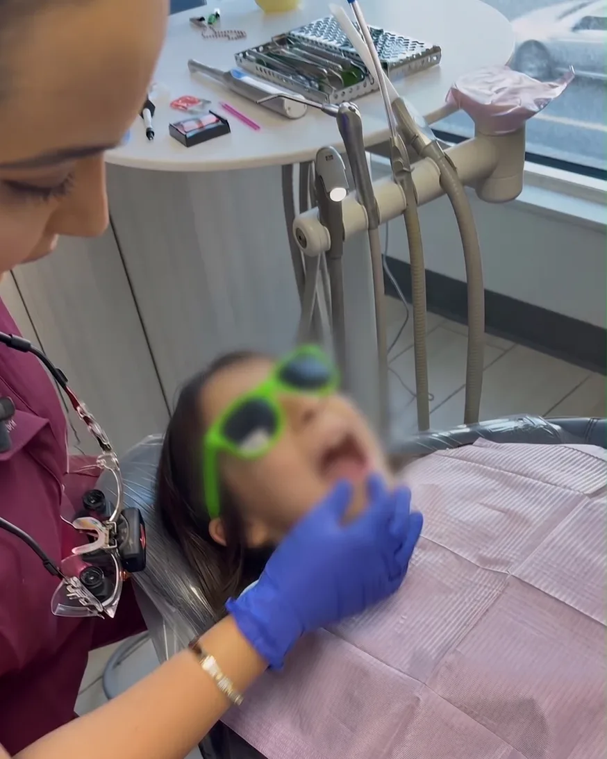 Dr. Nidhi checking a child's teeth, the child relaxed in the chair wearing bright sunglasses