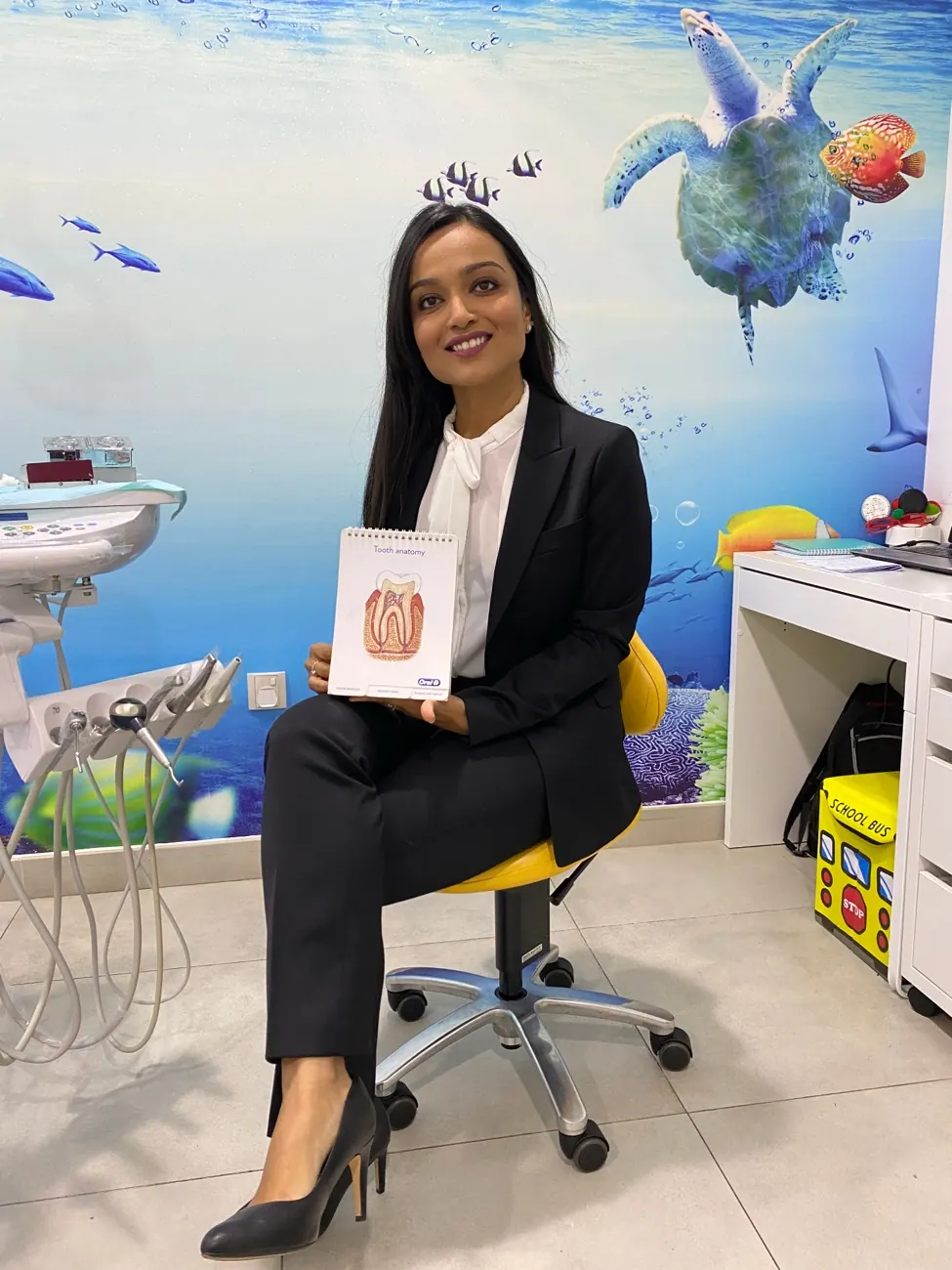 Dr. Nidhi in her clinic holding the tooth anatomy chart she uses to explain findings to parents