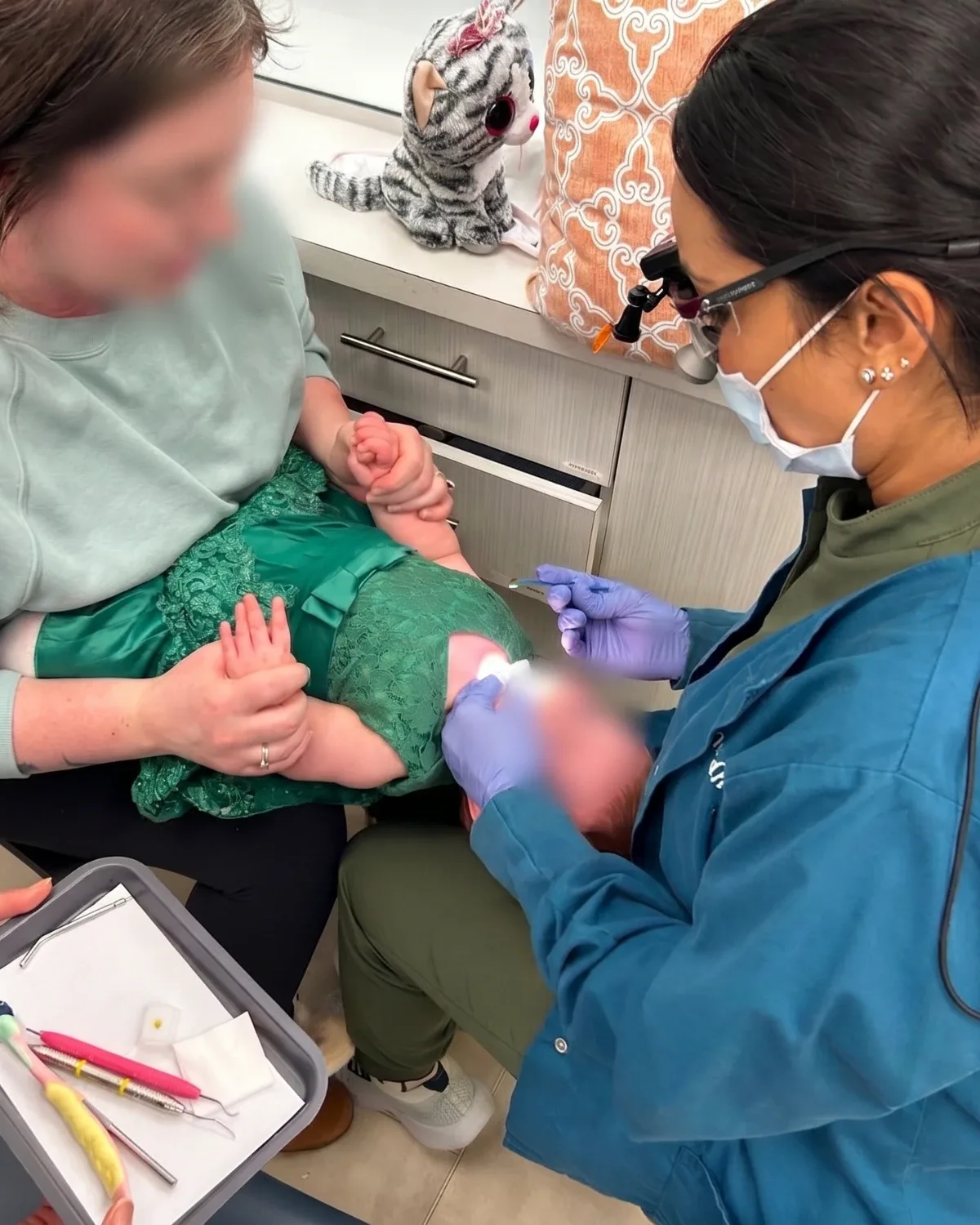 A knee-to-knee examination, the baby resting on a parent's lap while Dr. Nidhi checks her teeth