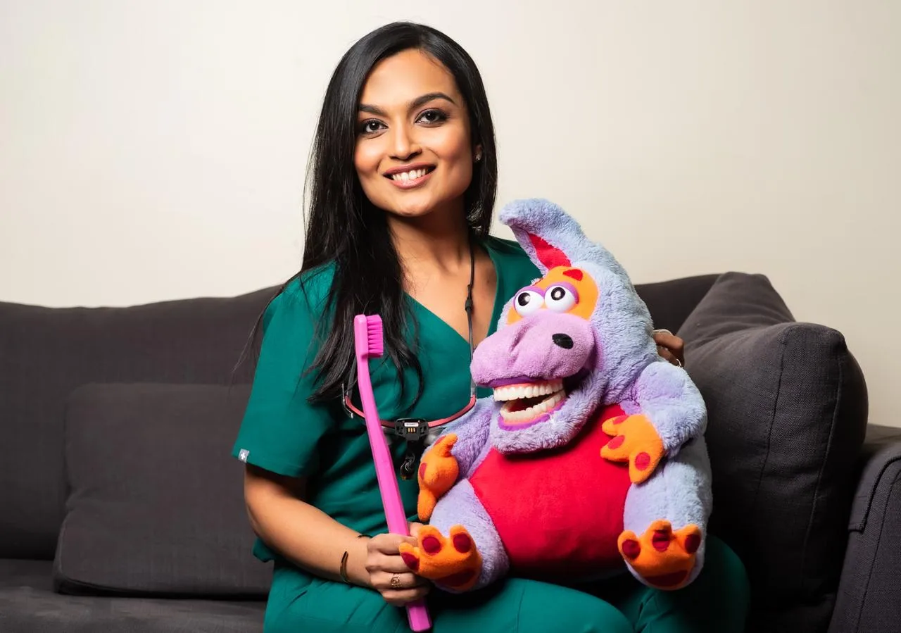 Dr. Nidhi holding her dinosaur puppet and an oversized toothbrush, the props she uses to show a child what happens before it happens