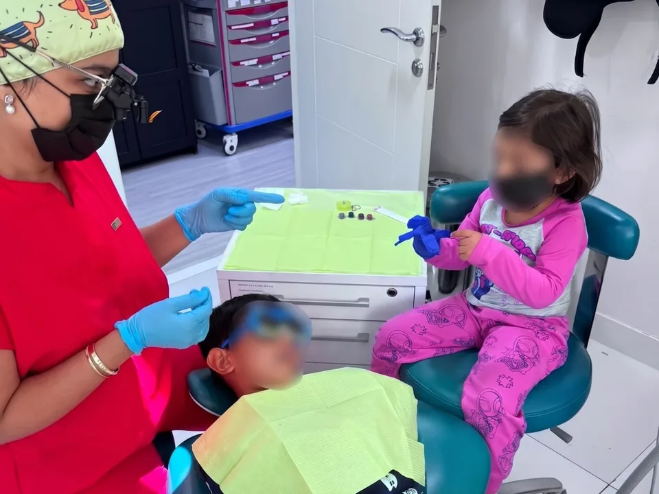 Dr. Nidhi checking a child's teeth while a sibling watches from the next chair